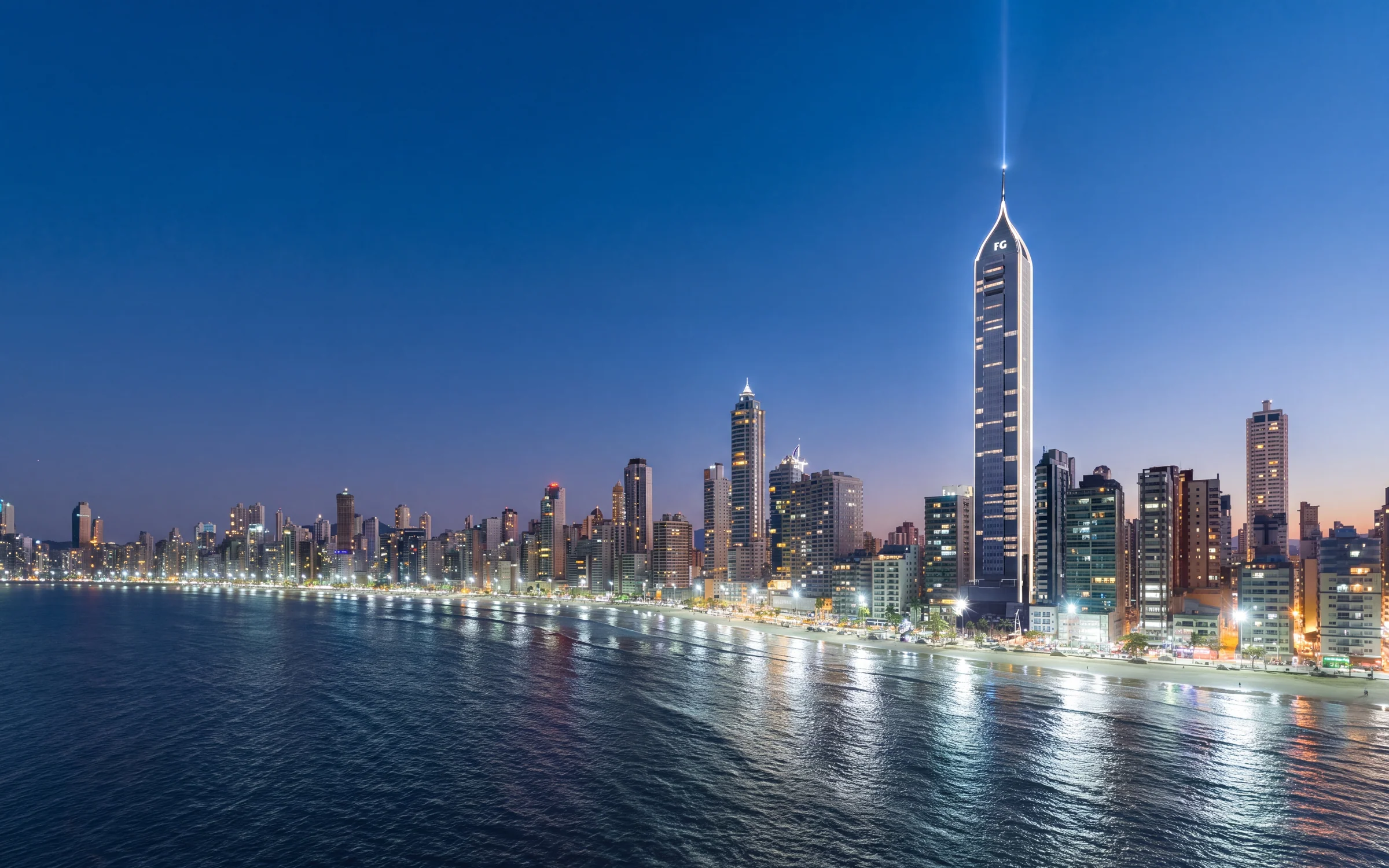 Titanium Tower iluminada junto à orla de Balneário Camboriú, com reflexos na água.